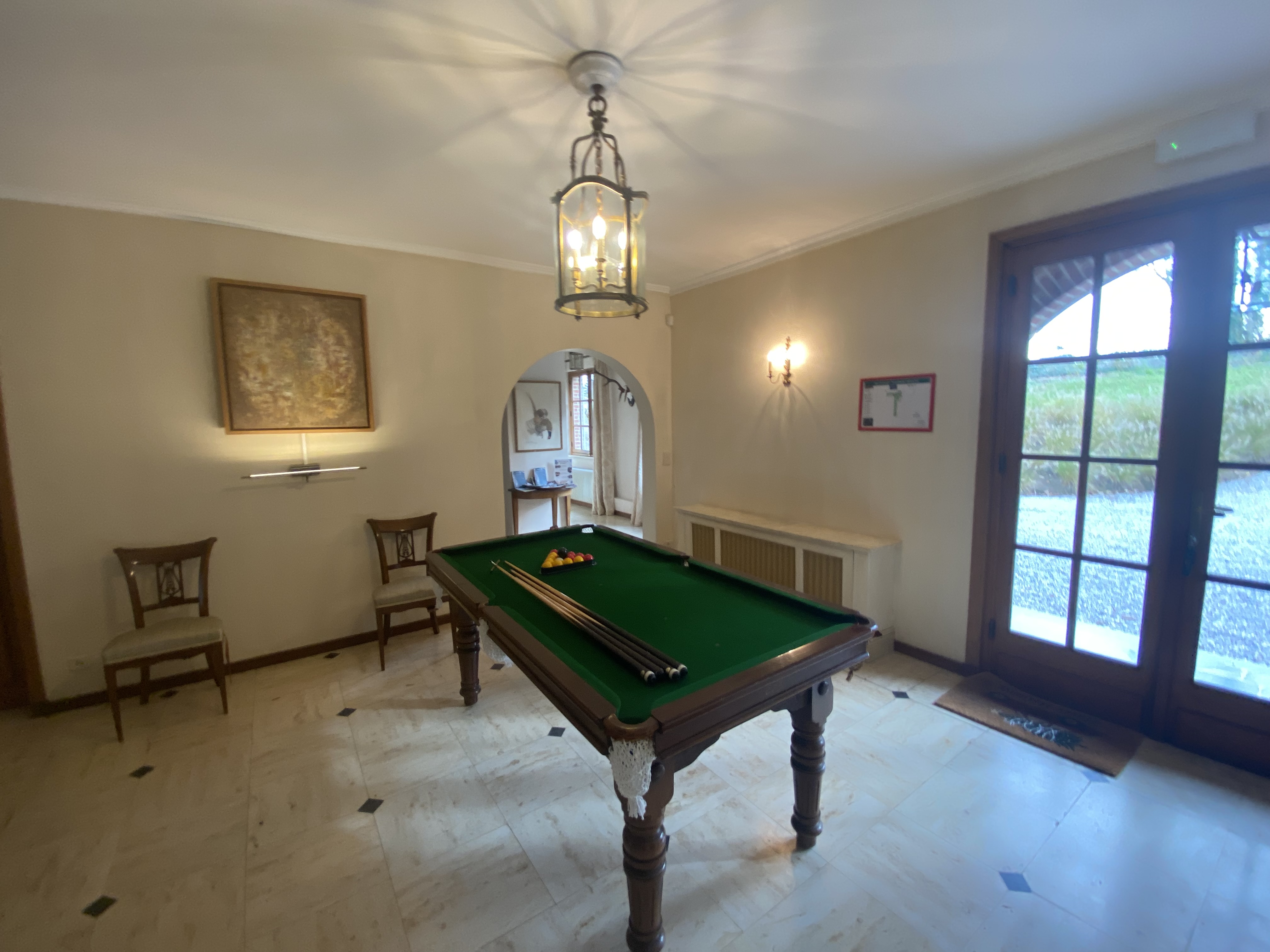 Salle de jeux avec table de billard, chaises en bois et sol en pierre