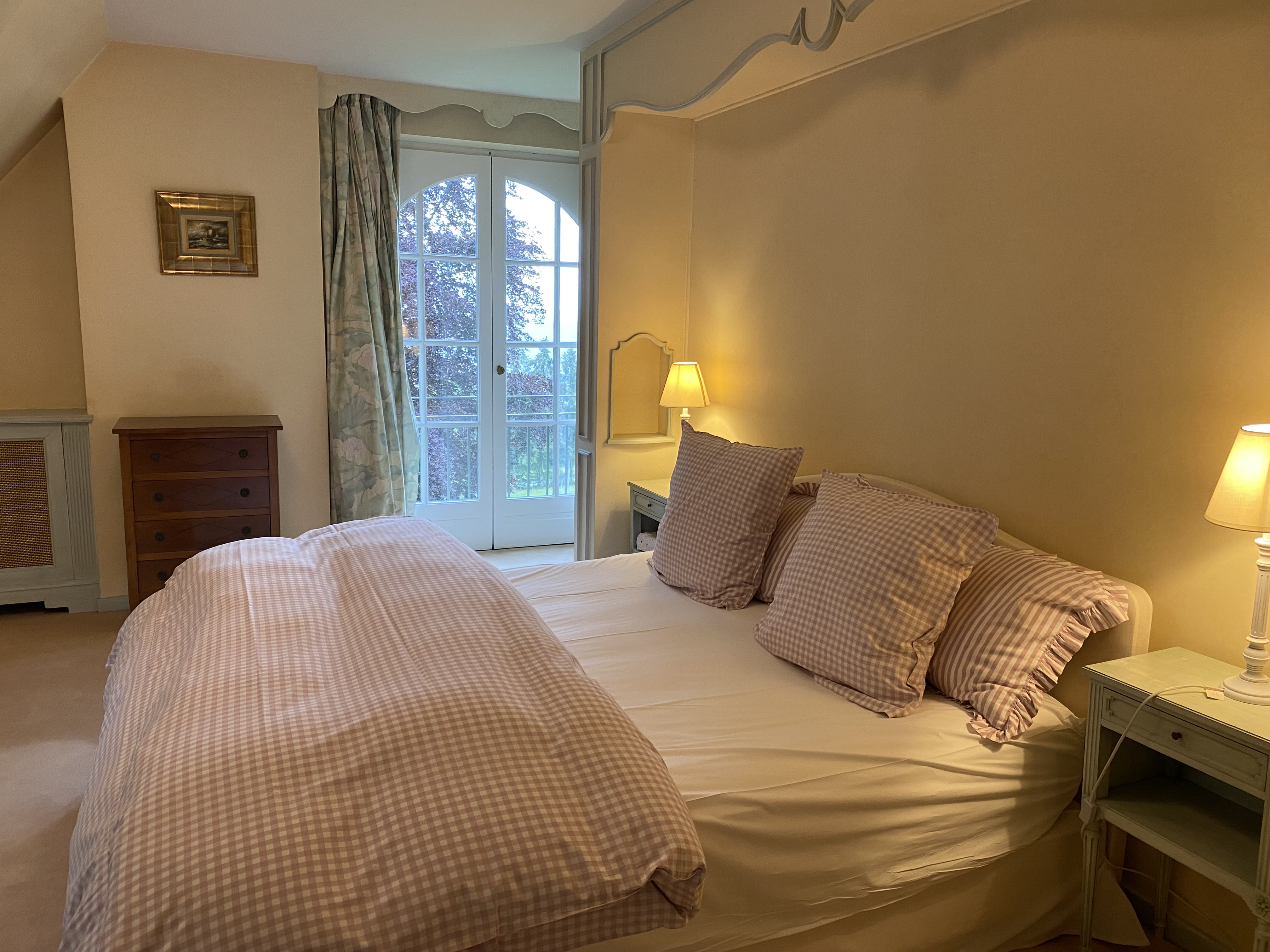 Chambre avec lit à carreaux roses, commode en bois et porte-fenêtre cintrée