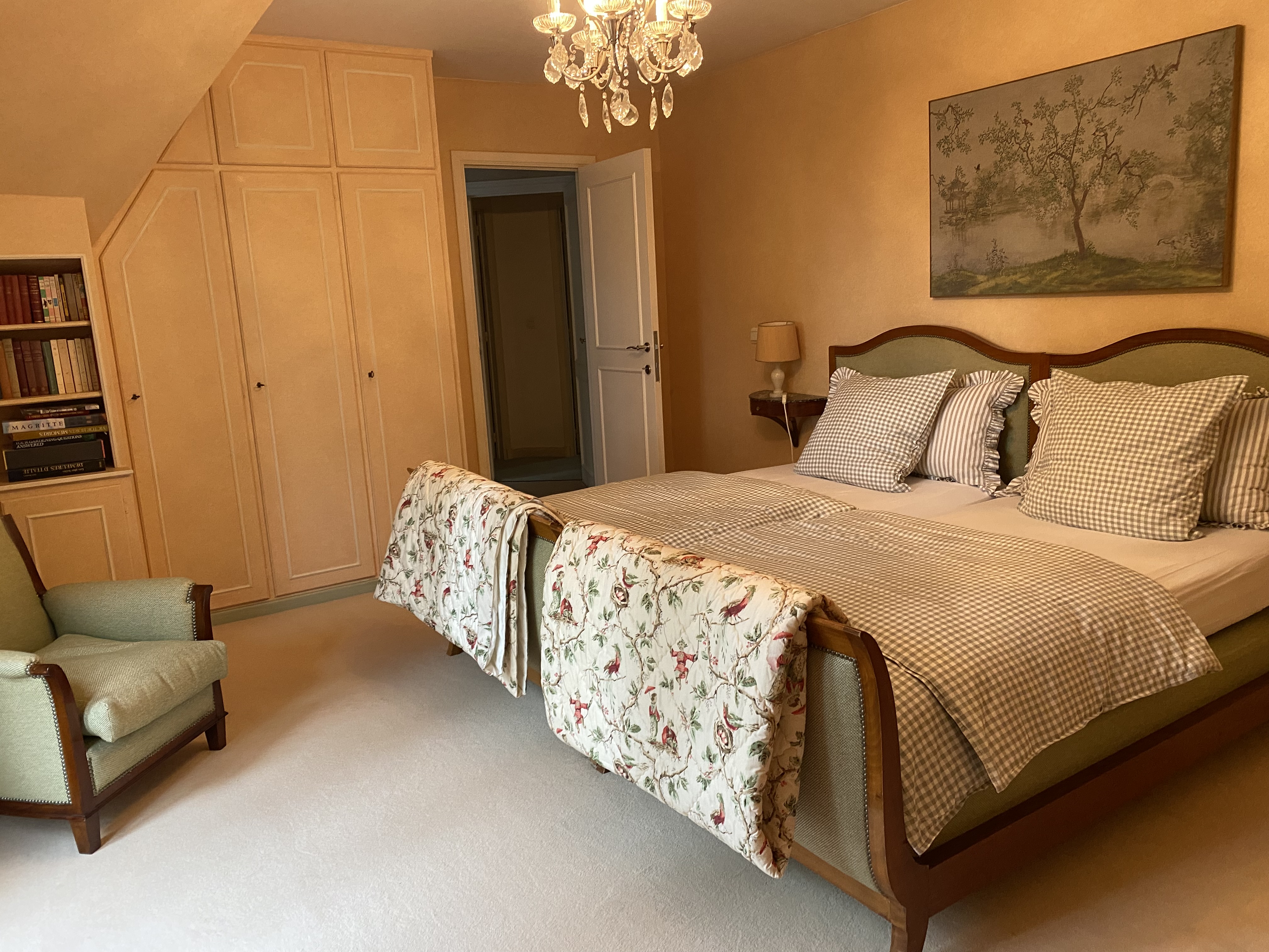 Chambre avec lits jumeaux, fauteuil vert et grande armoire intégrée