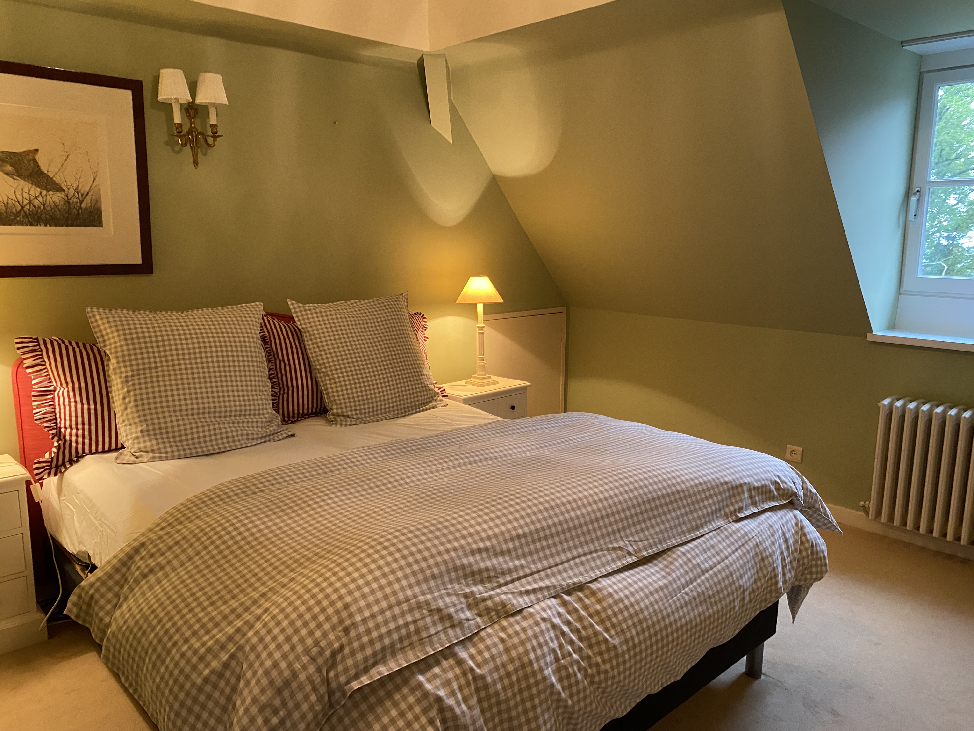 Chambre aux tons verts avec lit à carreaux et fenêtre sur la verdure