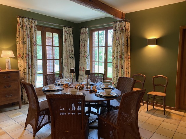 Salle à manger avec table ronde, chaises en osier et murs vert olive