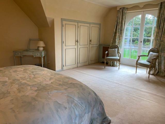 Chambre spacieuse avec coiffeuse, fauteuils et porte-fenêtre sur le jardin