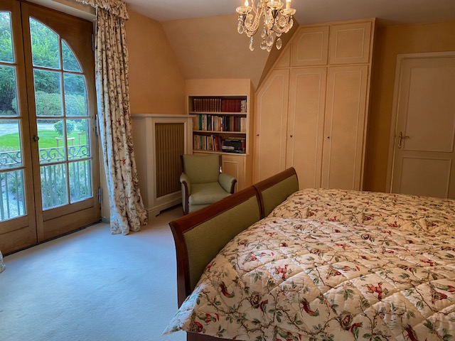Chambre élégante avec lit fleuri, fauteuil et bibliothèque sous les combles