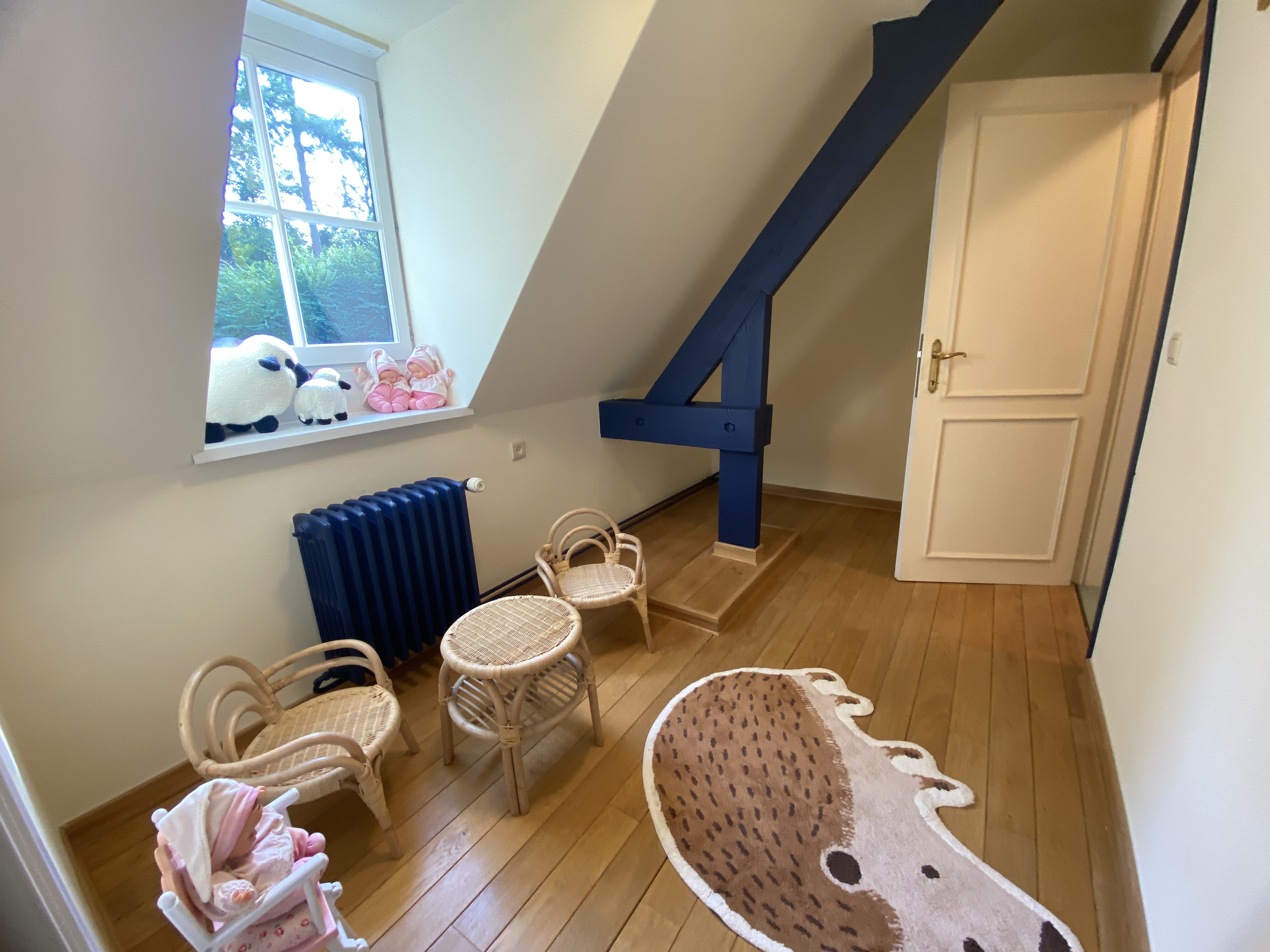 Coin jeux avec mobilier en rotin, tapis hérisson et peluches à la fenêtre