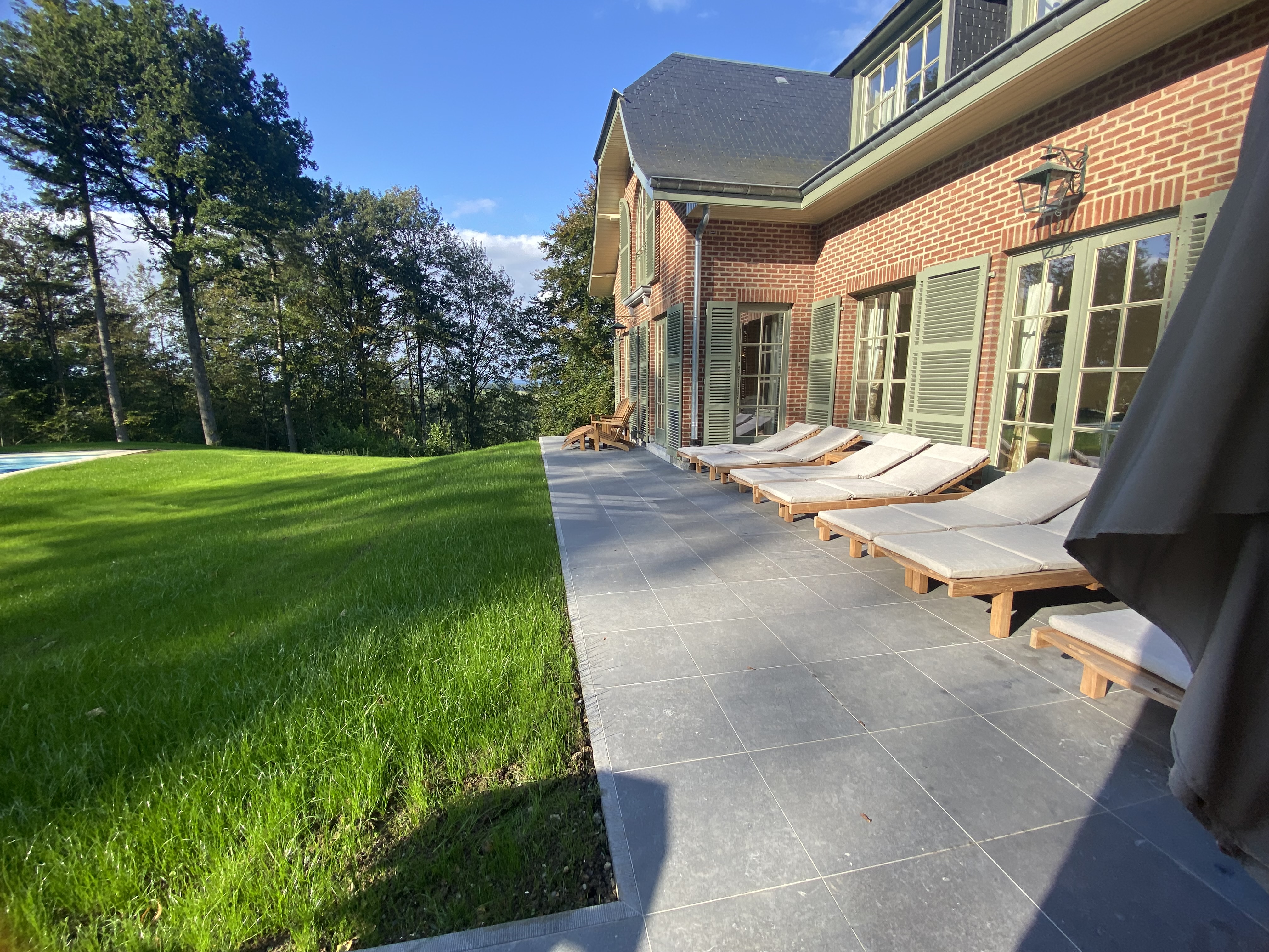 Terrasse ensoleillée avec chaises longues, jardin et vue sur la forêt