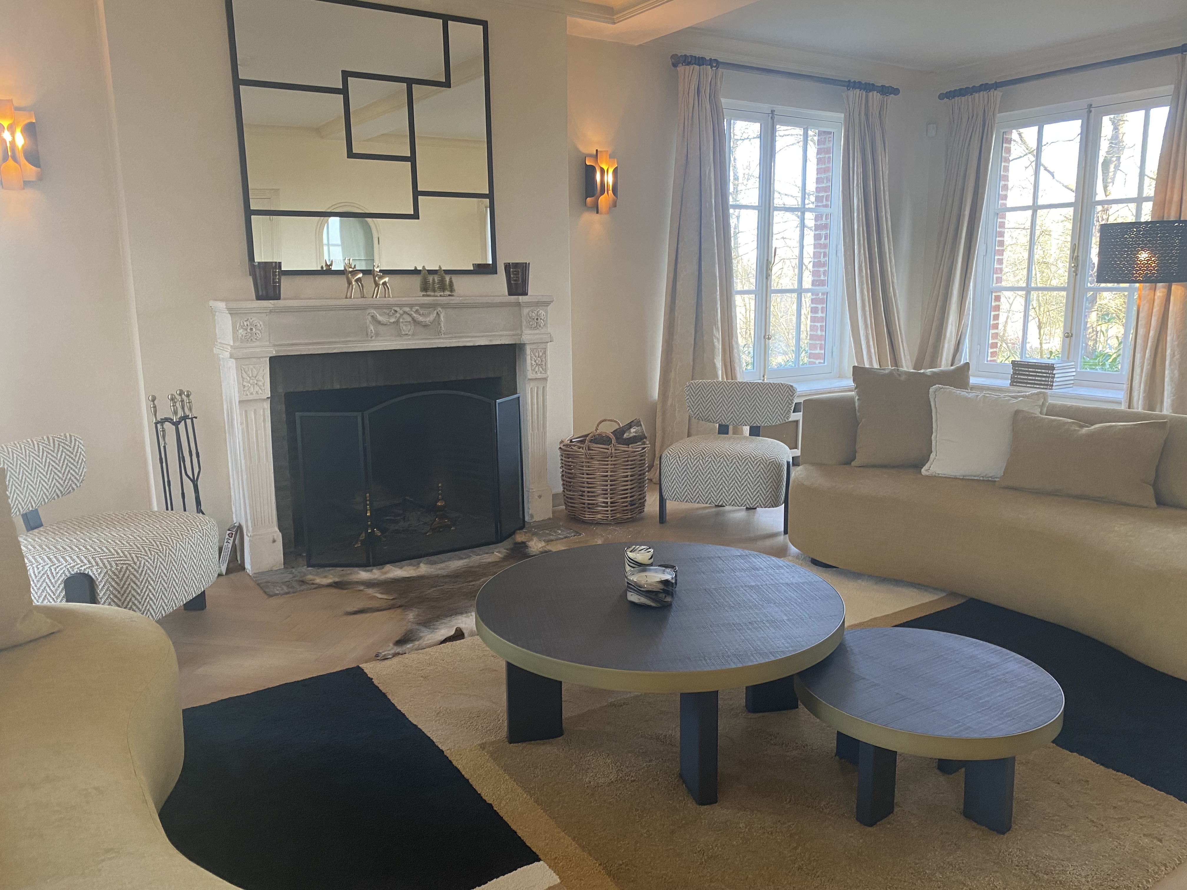 Salon avec cheminée, canapés arrondis moutarde, fauteuils à chevrons et tables circulaires