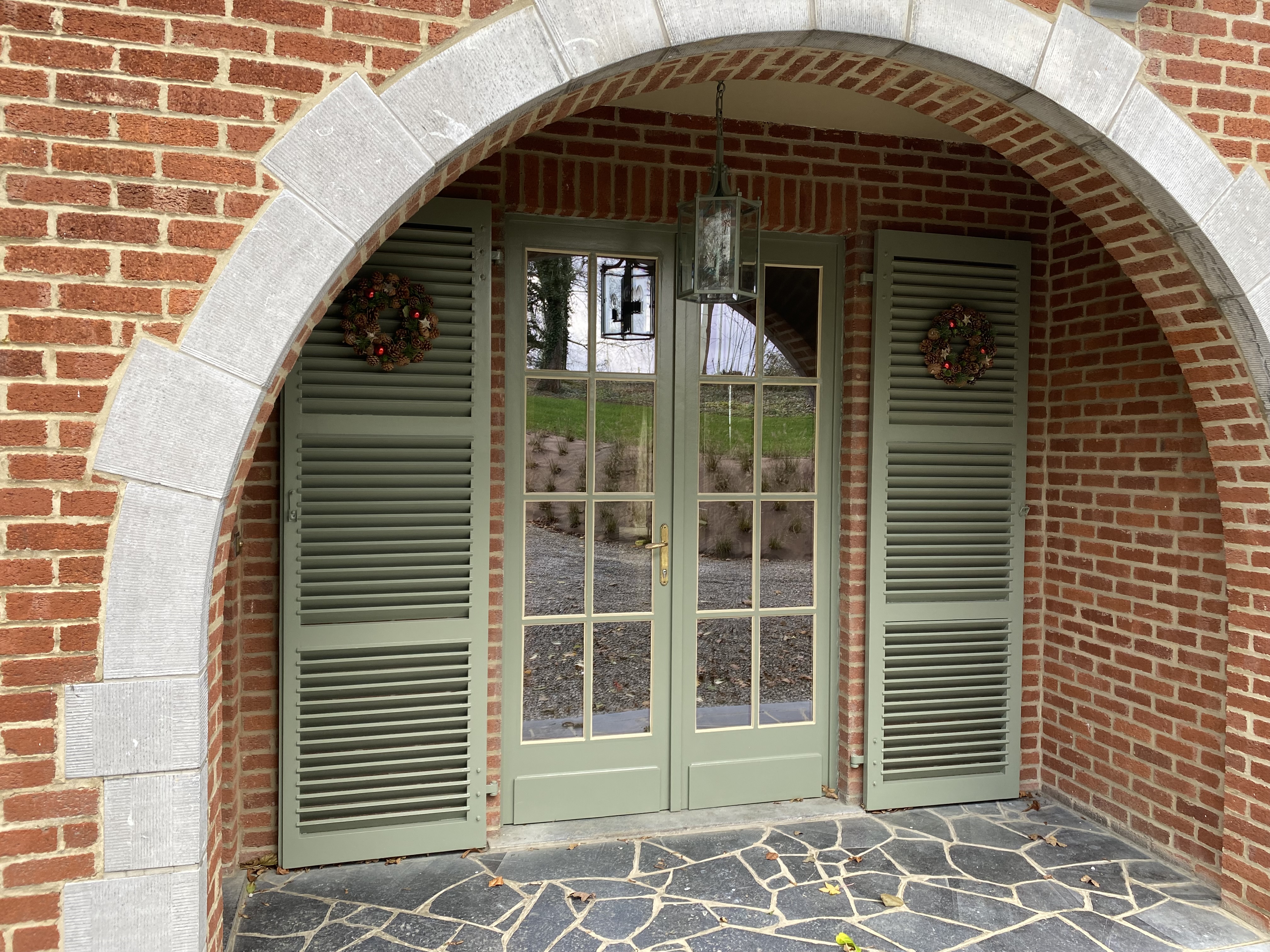 Entrée extérieure avec porte vitrée, volets verts et arche en pierre